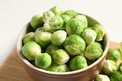 Photo of Bowl of fresh Brussels sprouts on wooden board, closeup