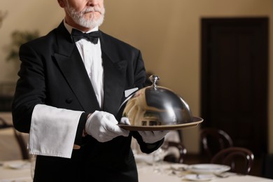 Photo of Butler holding metal tray with lid in restaurant, closeup. Space for text