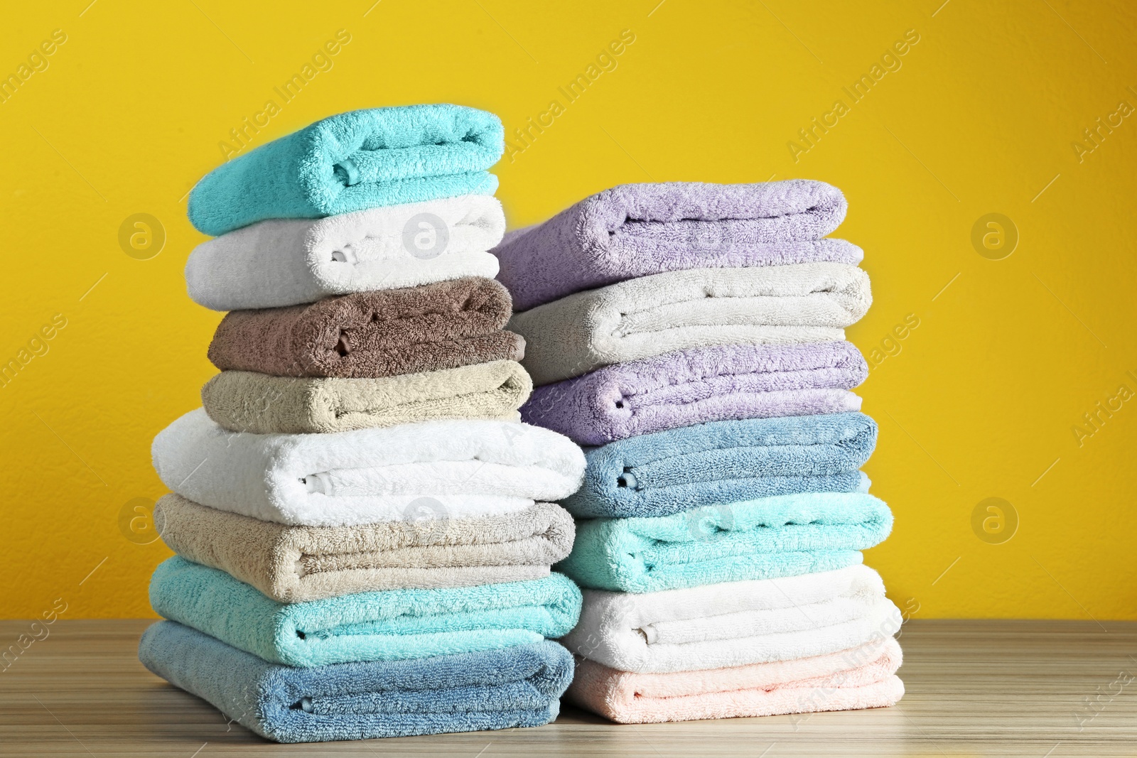 Photo of Different fresh soft terry towels on wooden table against yellow background