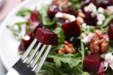 Fork with slice of beet near tasty salad, closeup