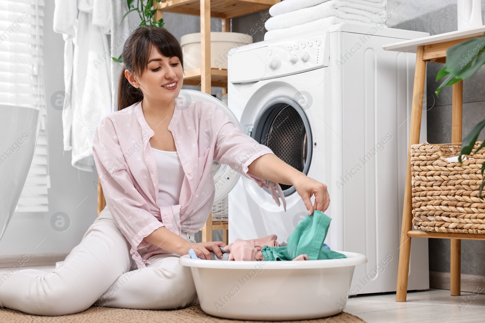 Photo of Young housewife with laundry near washing machine at home