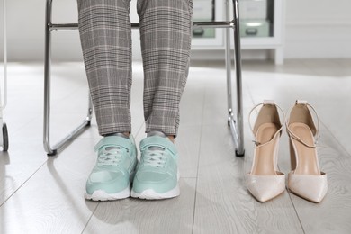 Photo of High heeled shoes near businesswoman wearing comfortable sneakers in office, closeup