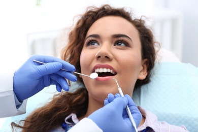 Dentist examining African-American woman's teeth with probe and mirror in hospital