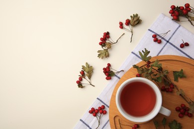 Cup with hawthorn tea and berries on beige table, flat lay. Space for text