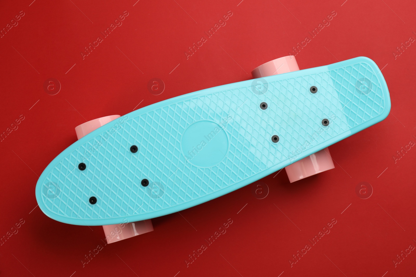Photo of Turquoise skateboard on red background, top view