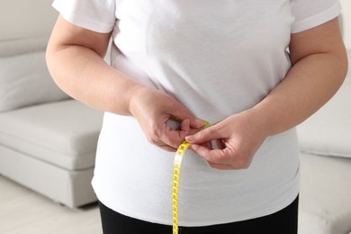 Overweight woman measuring waist with tape at home, closeup