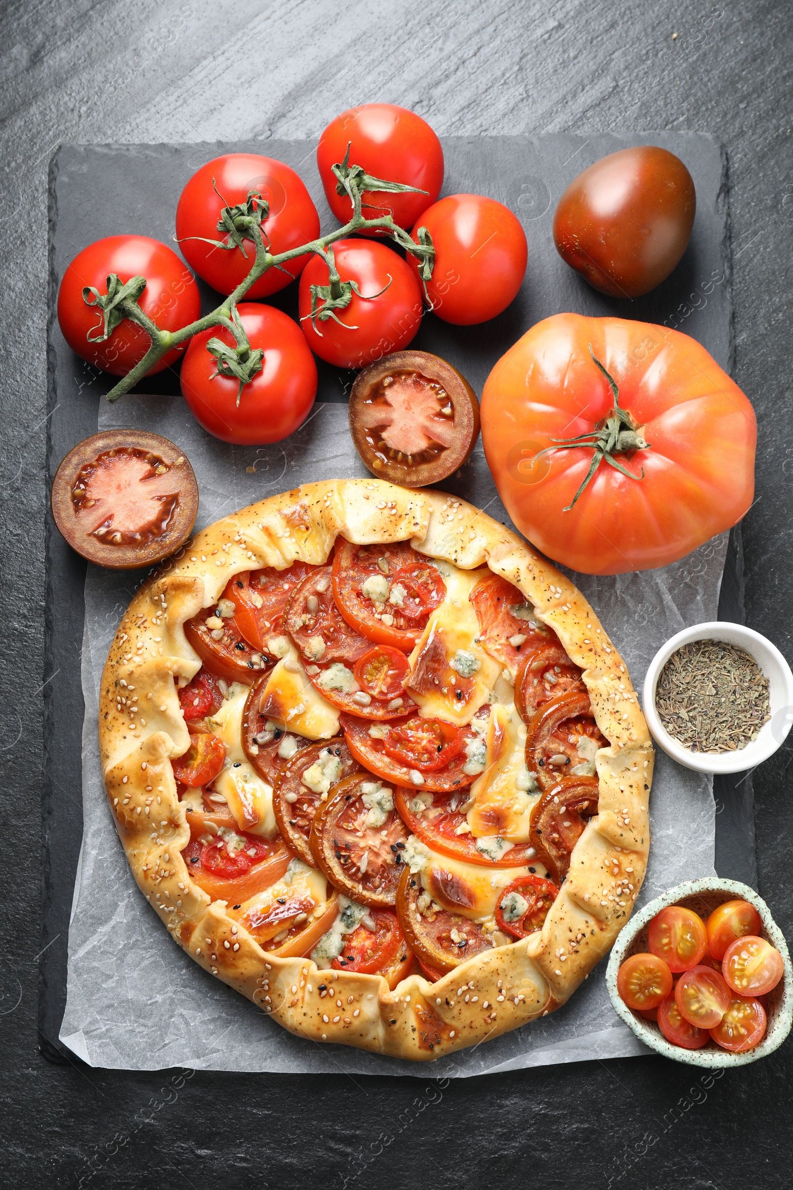 Photo of Tasty galette with tomato and cheese (Caprese galette) on dark textured table, top view