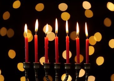 Photo of Golden menorah with burning candles against dark background and blurred festive lights
