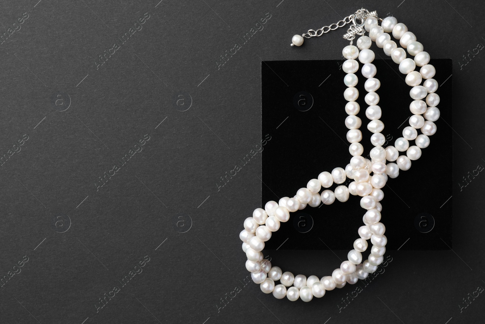 Photo of Elegant pearl necklace on black background, top view. Space for text