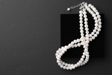 Elegant pearl necklace on black background, top view. Space for text