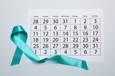 Photo of Teal awareness ribbon and calendar on white background, top view. Symbol of social and medical issues