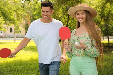 Happy couple with tennis rackets and ball near ping pong table in park
