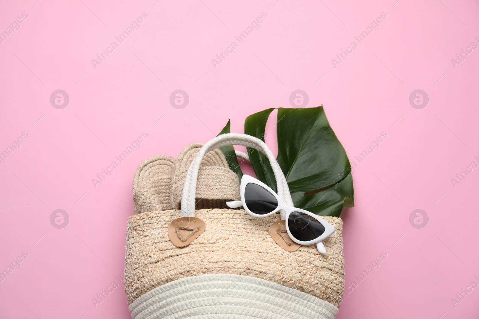 Photo of Elegant woman's straw bag with shoes, tropical leaf and sunglasses on pink background, top view