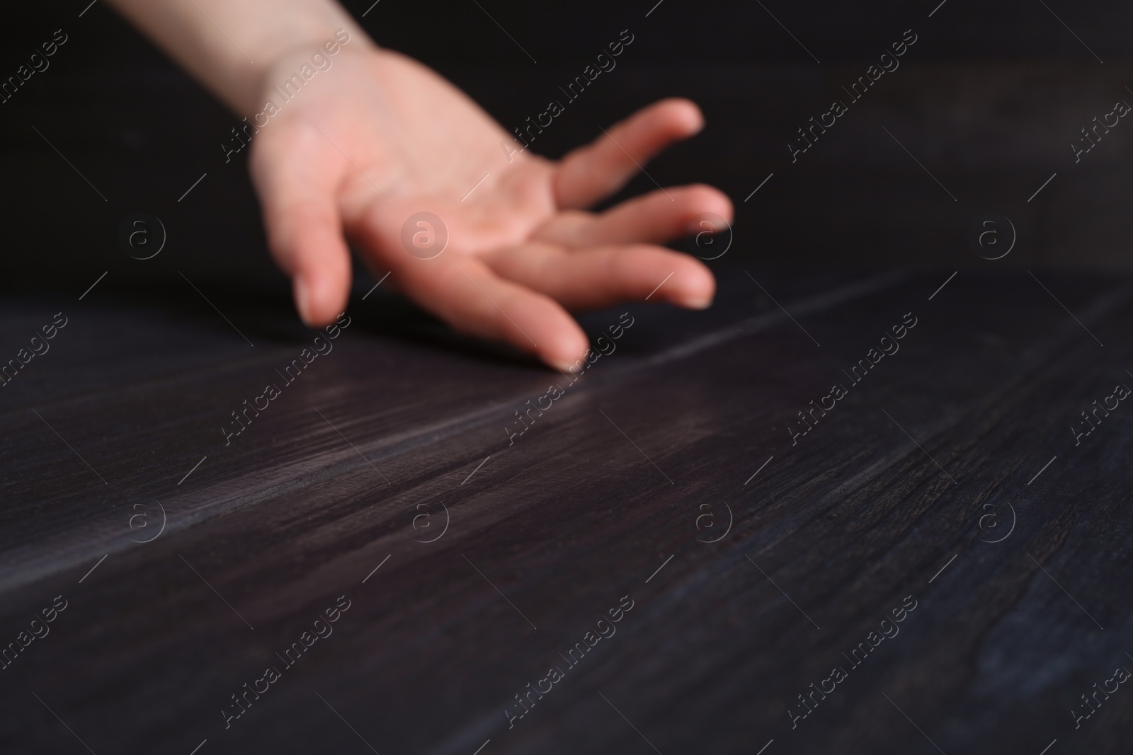 Photo of Woman holding hand above black wooden table, selective focus. Space for text