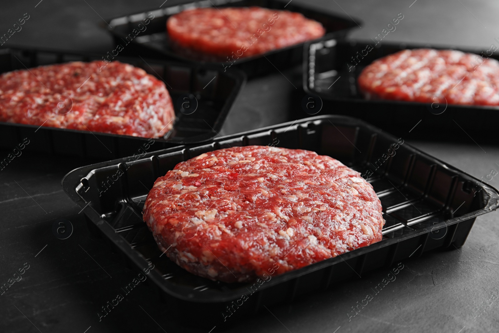 Photo of Plastic containers with raw meat cutlets for burger on grey table, closeup