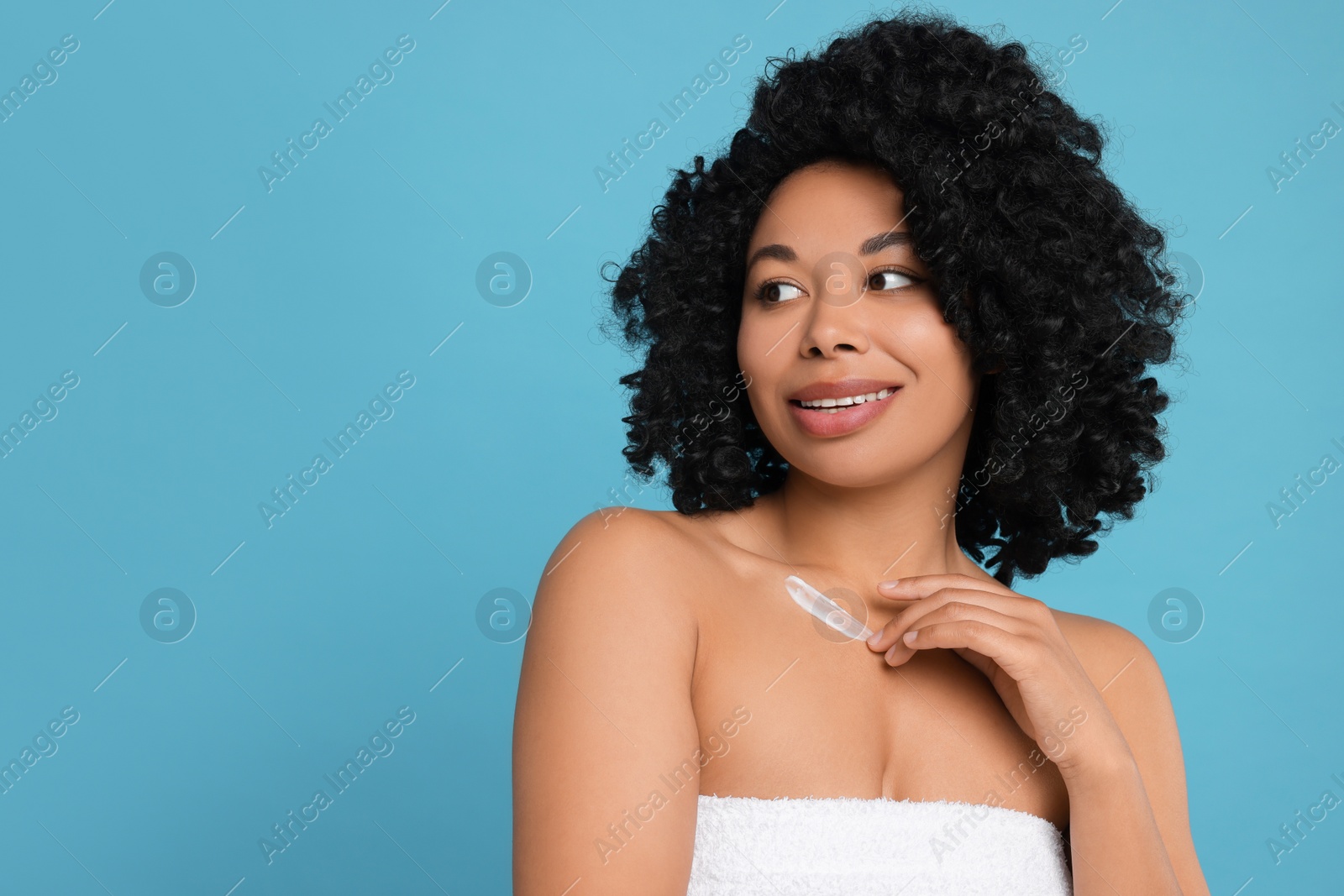 Photo of Young woman applying cream onto body on light blue background. Space for text