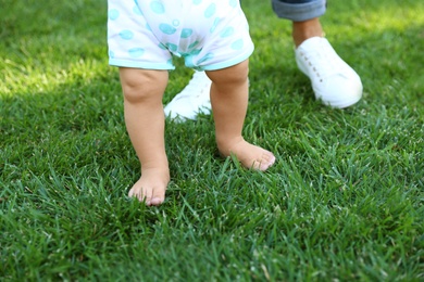 Photo of Cute little baby learning to walk with his nanny on green grass outdoors, closeup