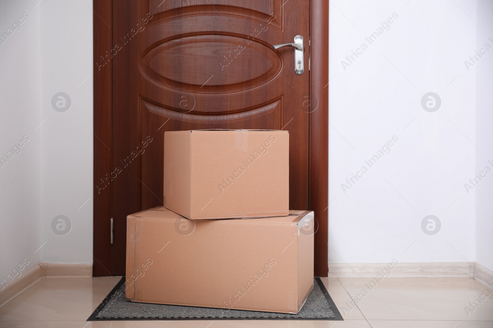 Photo of Cardboard boxes on rug near door. Parcel delivery service