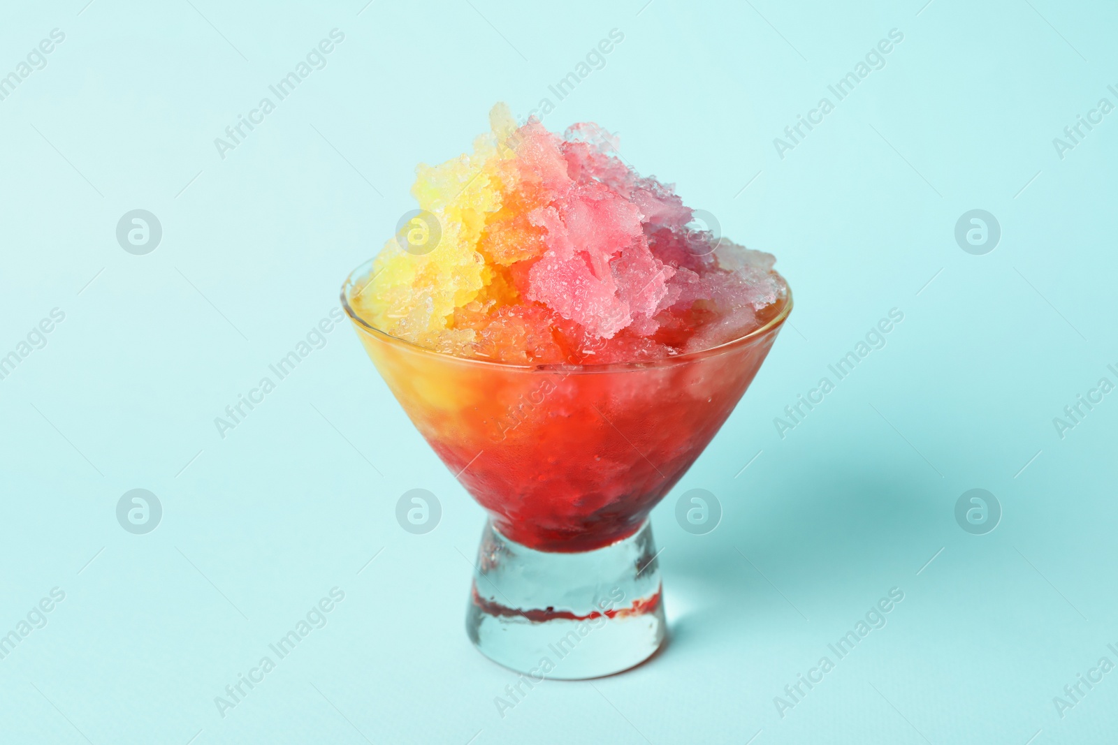 Photo of Rainbow shaving ice in glass dessert bowl on light blue background, closeup