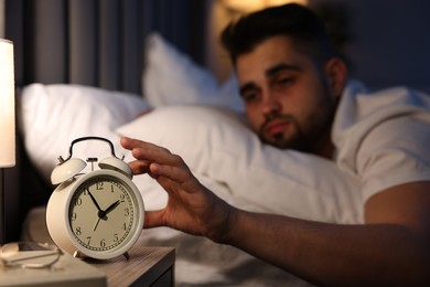 Photo of Sleepy man turning off alarm clock in bedroom, selective focus