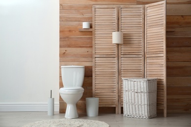 Photo of Toilet bowl near wooden wall in modern bathroom interior