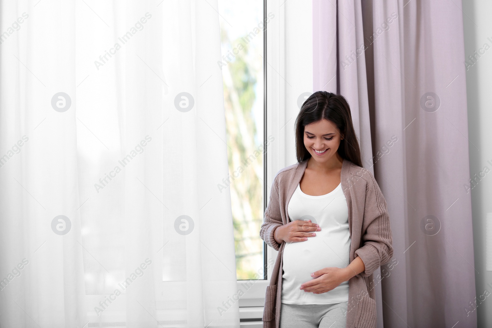 Photo of Happy pregnant woman standing near window at home