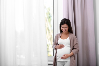 Photo of Happy pregnant woman standing near window at home