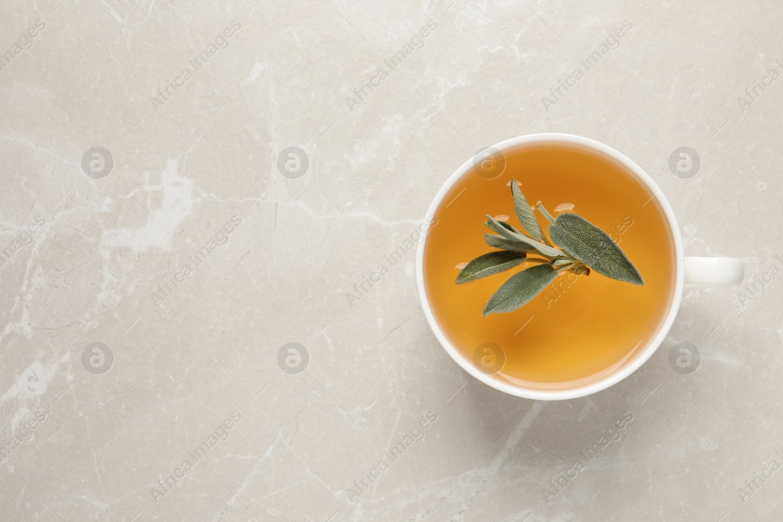 Photo of Cup of sage tea and green leaves on light grey table, top view. Space for text