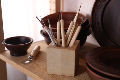 Set of different crafting tools and clay dishes on wooden rack in workshop