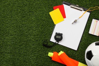 Soccer ball and different referee equipment on green grass, flat lay. Space for text