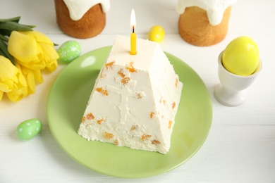 Photo of Traditional cottage cheese Easter paskha with dried apricot and burning candle on white wooden table
