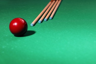 Red billiard ball and cues on table. Space for text