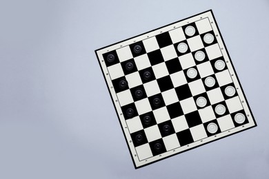 Photo of Black and white checkerboard with game pieces on light grey background, top view. Space for text