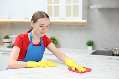 Photo of Woman cleaning white marble table with rag in kitchen, space for text