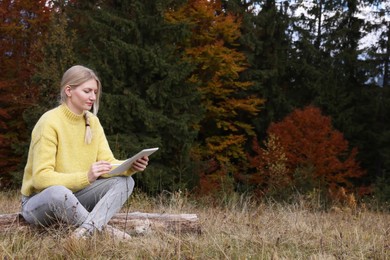 Young woman drawing with graphic tablet near forest in autumn