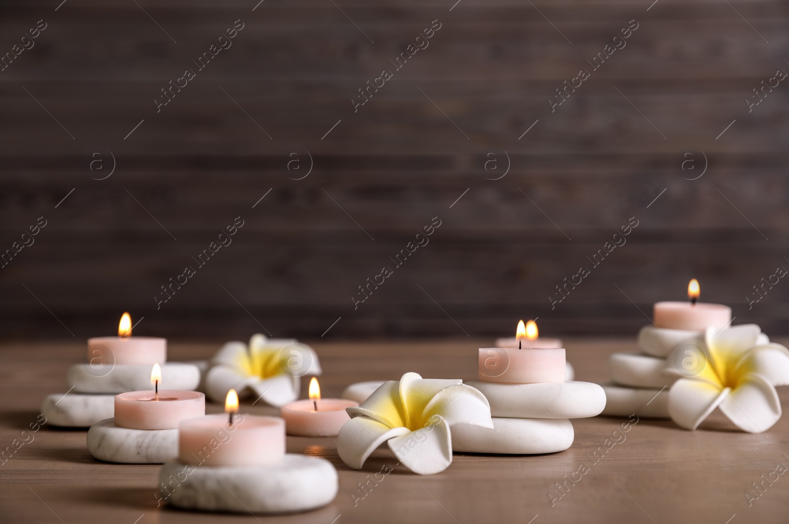 Photo of Composition of spa stones, flowers and burning candles on wooden table