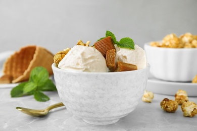 Photo of Bowl of delicious ice cream with caramel candies, popcorn and mint on light grey marble table