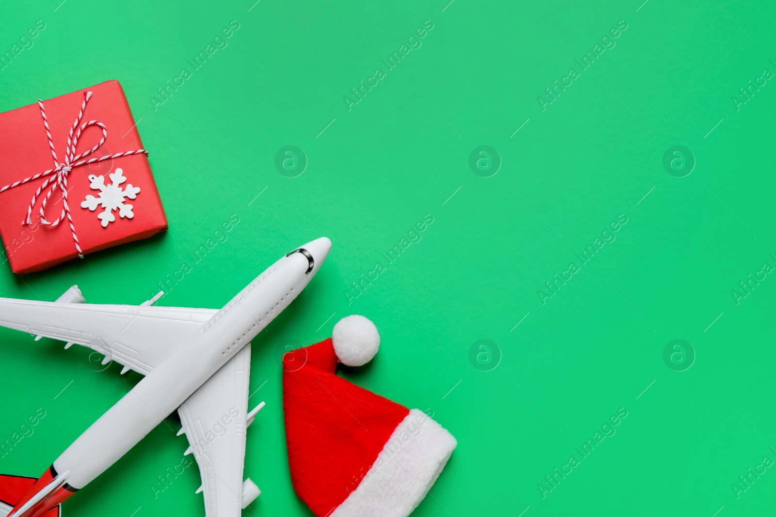 Photo of Santa hat, toy airplane, gift box and space for text on green background, flat lay. Christmas vacation