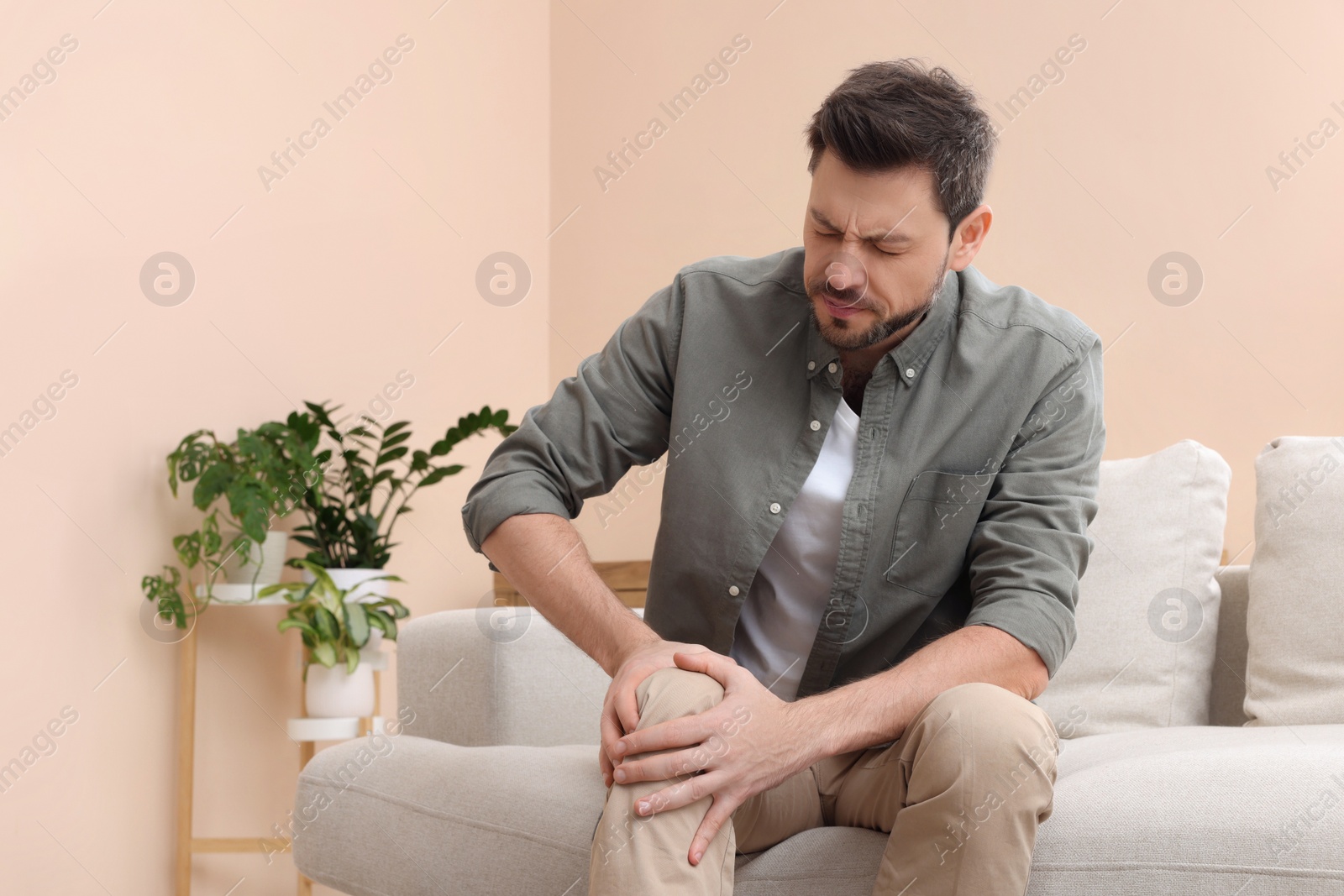 Photo of Man suffering from pain in his leg at home, space for text. Arthritis symptoms