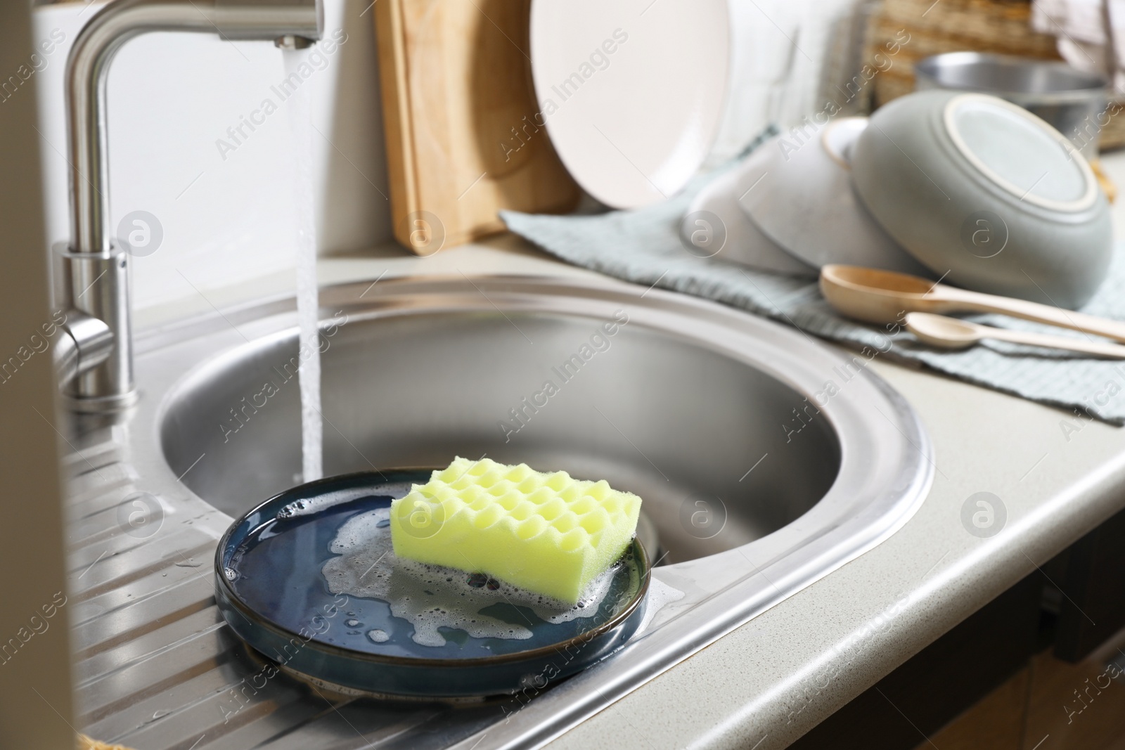 Photo of Plate and sponge in kitchen sink. Washing dishes