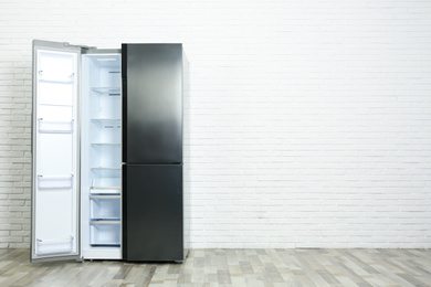 Photo of Modern empty refrigerator near white brick wall, space for text