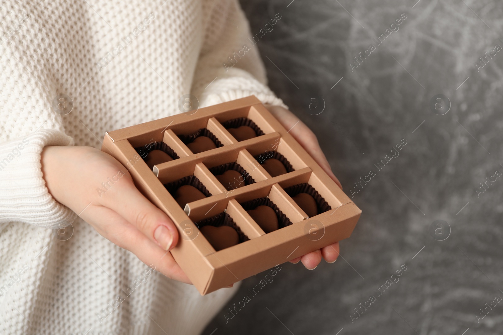 Photo of Woman with box of heart shaped chocolate candies on grey background, closeup