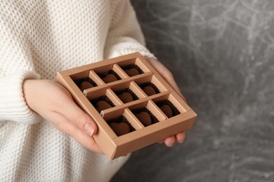 Woman with box of heart shaped chocolate candies on grey background, closeup