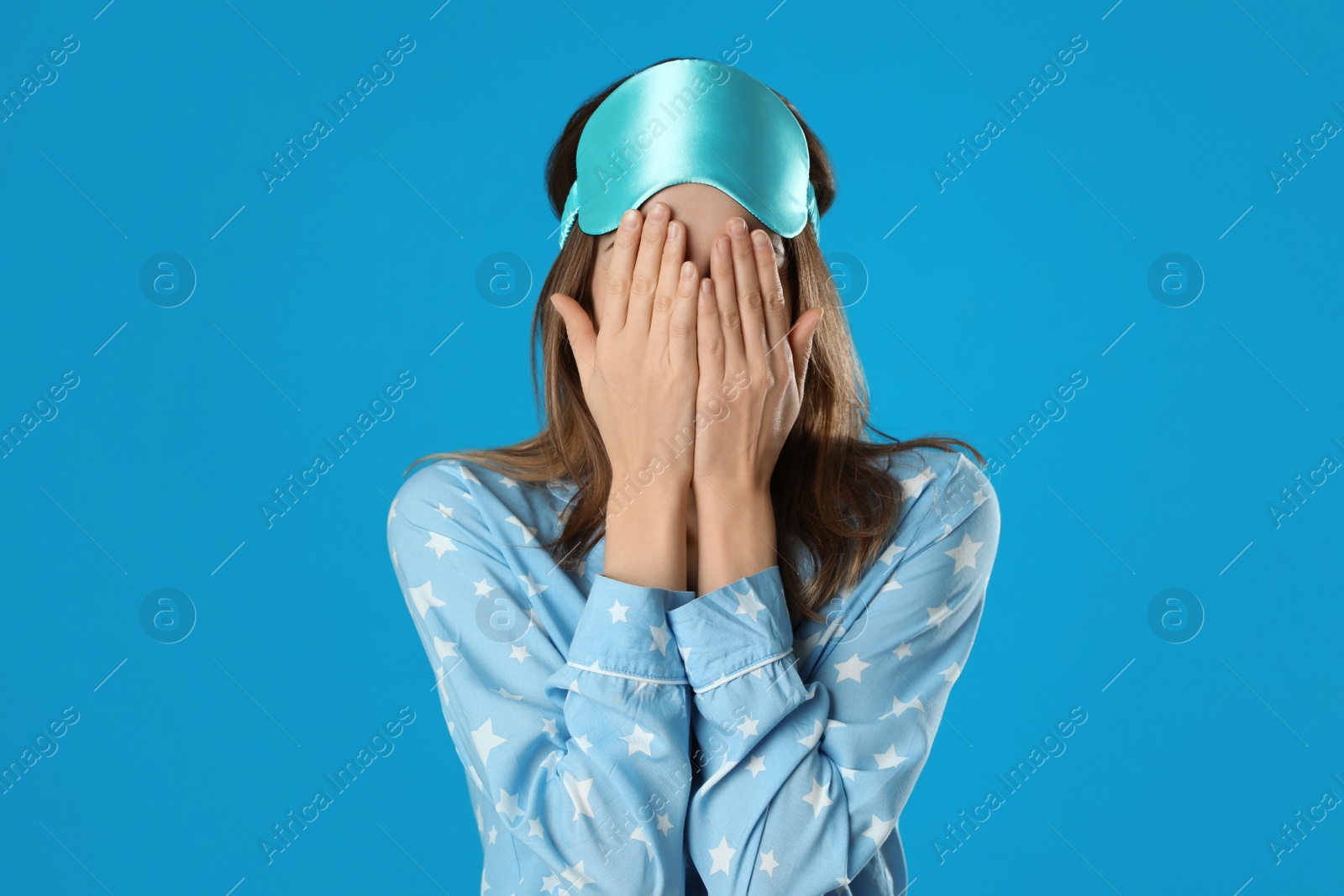 Photo of Beautiful woman wearing pajamas and sleep mask on light blue background. Bedtime