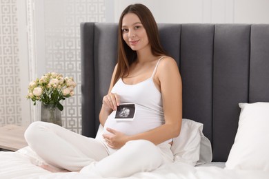 Pregnant woman with ultrasound picture of baby on bed indoors