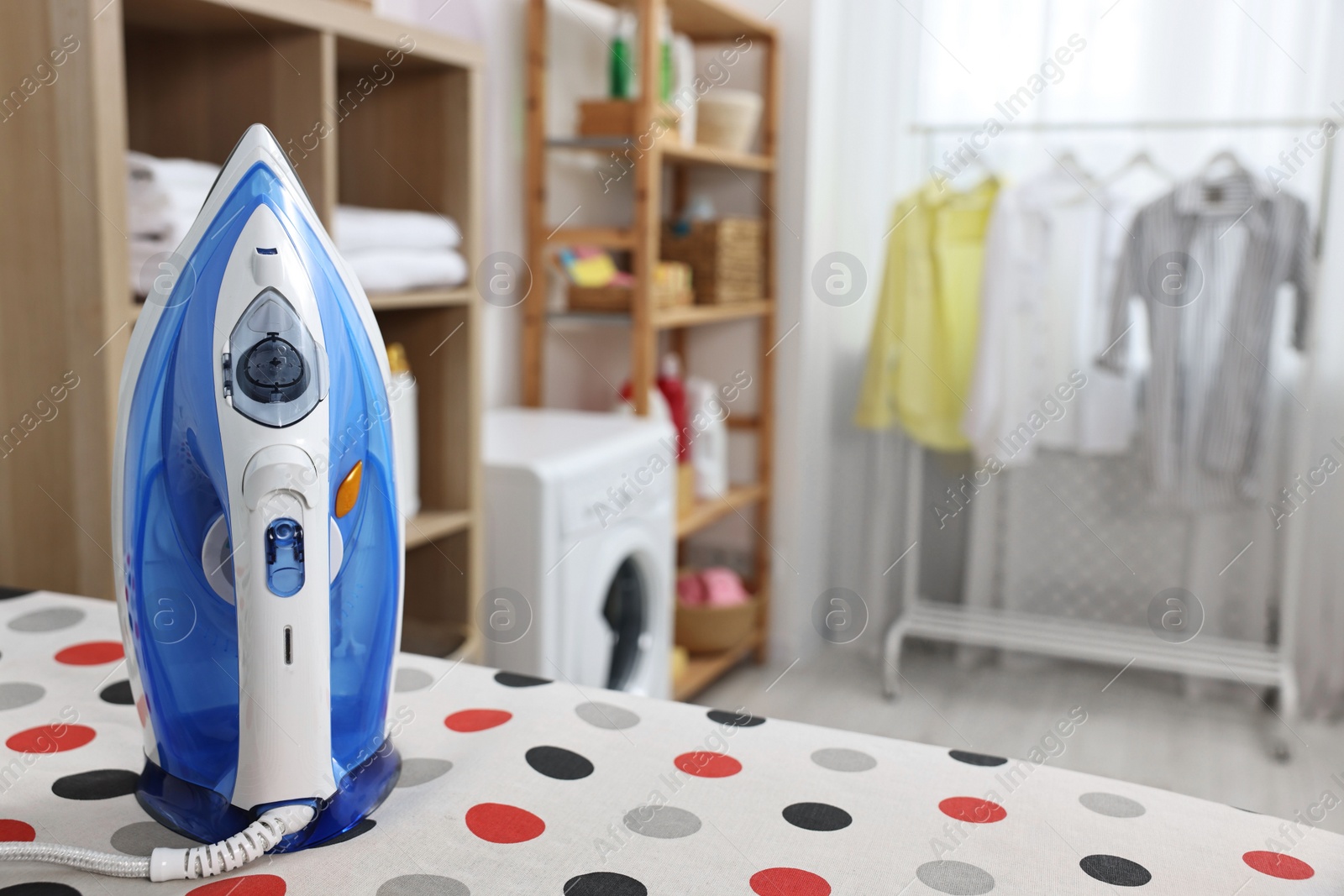 Photo of Clothes iron on ironing board in laundry room, space for text