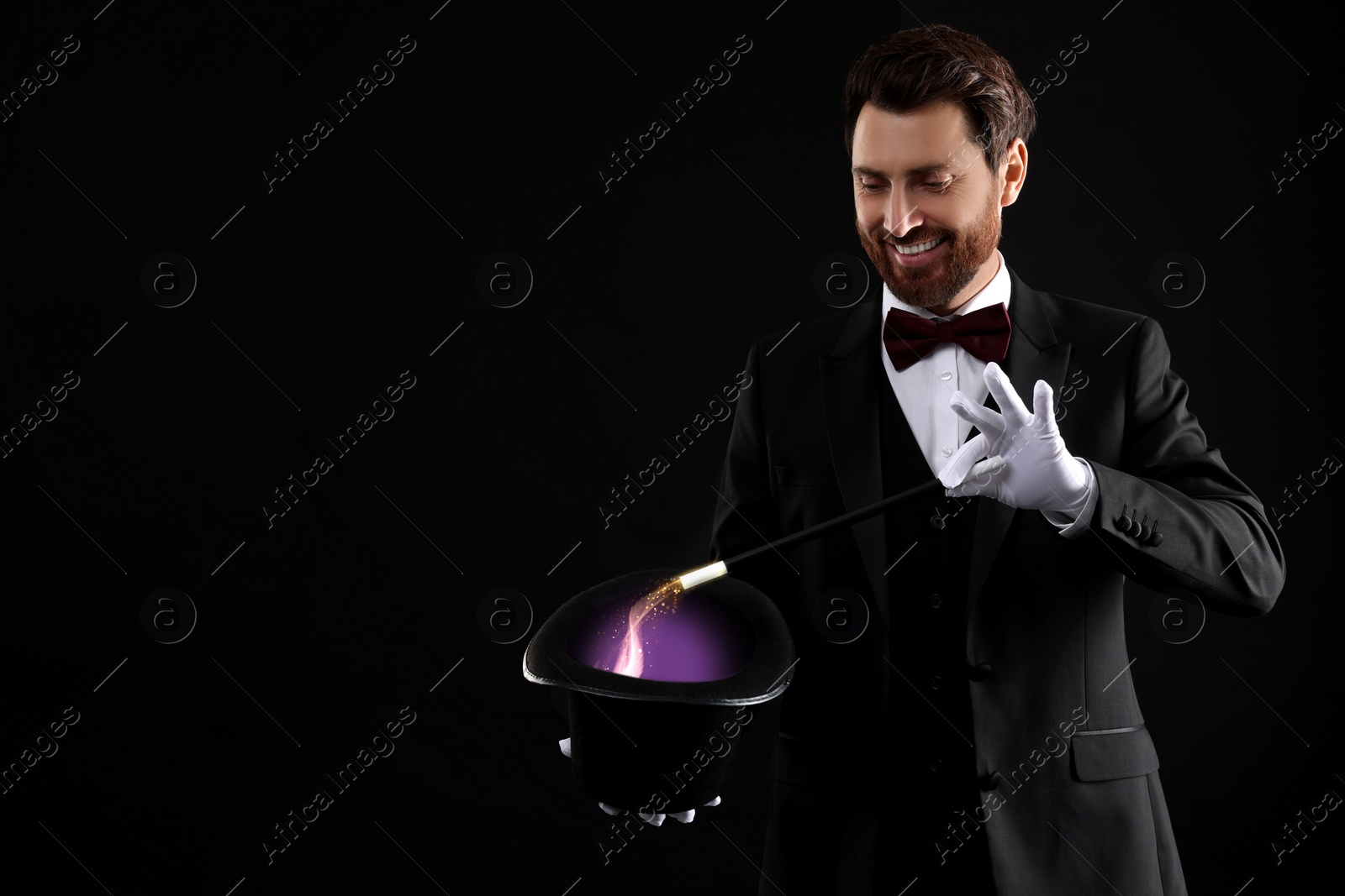 Image of Magician showing trick with wand and top hat on dark background. Fantastic light coming out of hat