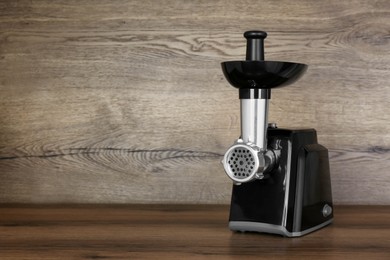 Modern electric meat grinder on wooden table. Space for text