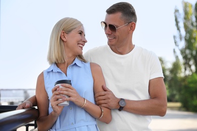 Happy couple with drink walking along city street on summer day