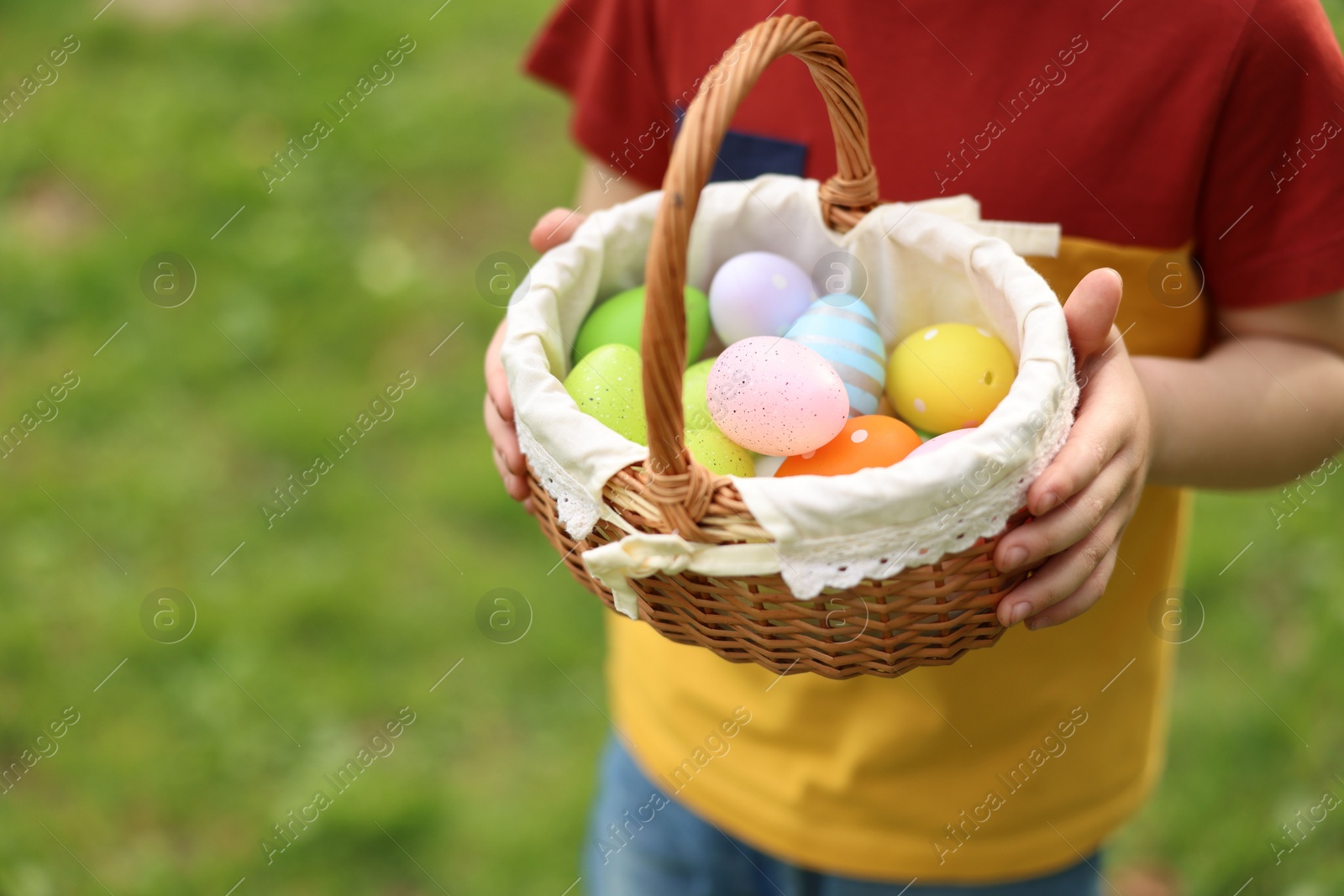 Photo of Easter celebration. Little boy holding basket with painted eggs outdoors, closeup. Space for text